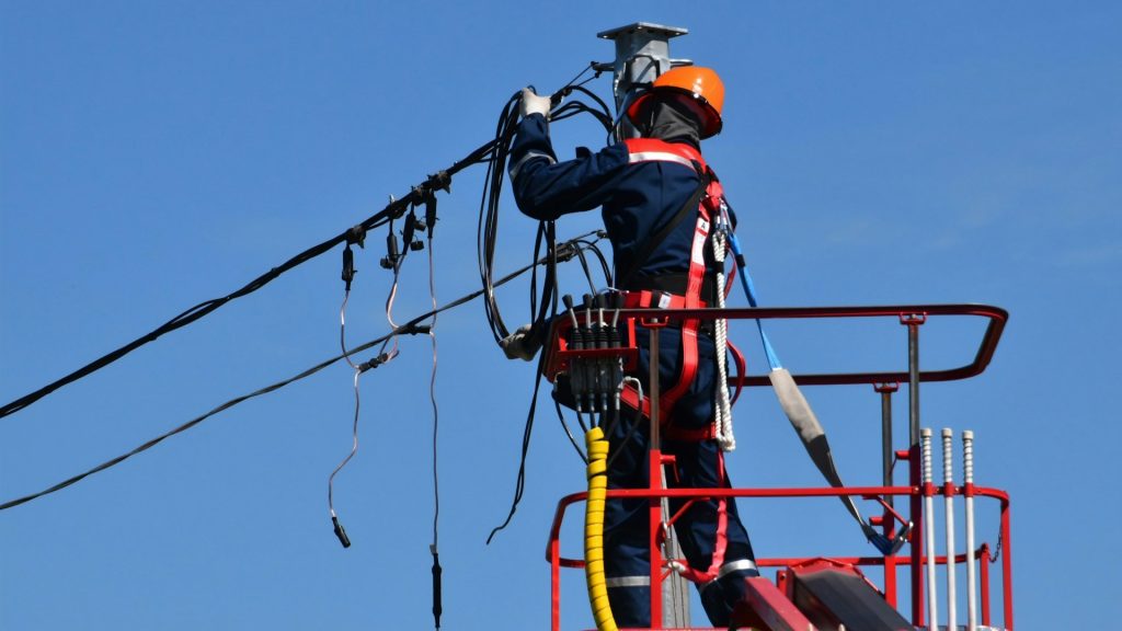 Technisch specialist op hoogte werkt aan elektriciteitsnet – weerspiegeling van het tekort aan monteurs.
